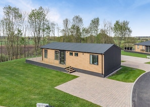 A modern, single-story wooden cabin with a dark roof, a small deck, and a paved driveway.