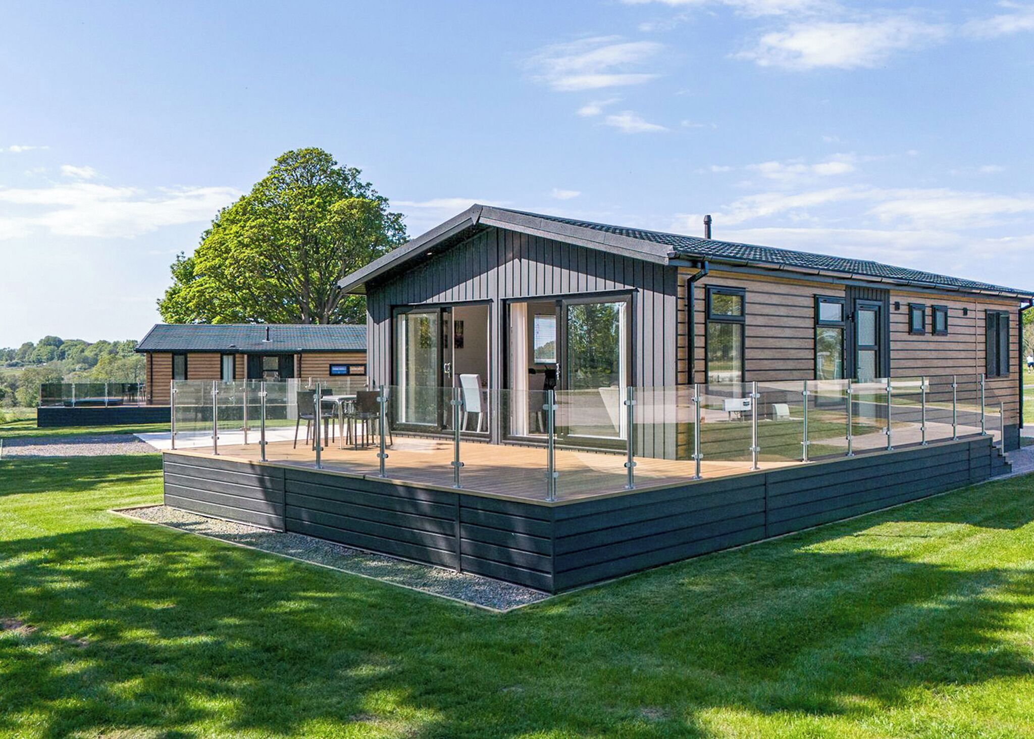 A modern wooden cabin with a glass-enclosed patio, a deck, and a view of the surrounding landscape.