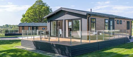 A modern wooden cabin with a glass-enclosed patio, a deck, and a view of the surrounding landscape.