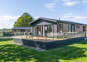 A modern wooden cabin with a glass-enclosed patio, a deck, and a view of the surrounding landscape.