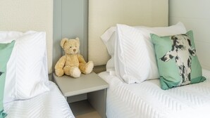 Un dormitorio con dos camas, una mesita de noche, un osito de peluche y almohadas decorativas.