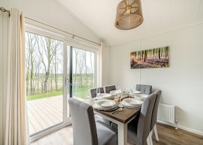 A dining area with a table set for four, a view of the outdoors through large windows, and a ceiling light fixture.