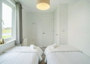 Une chambre d’hôtel avec deux lits, une fenêtre avec des rideaux, une porte et un luminaire suspendu.