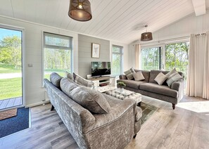 A spacious living room with a large sofa, a smaller sofa, a coffee table, and a TV on a white cabinet.