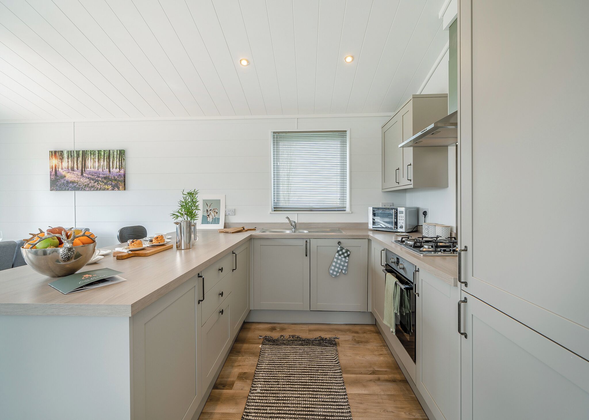 A modern kitchen with a wooden countertop, a bowl of fruit, a toaster, and a window with blinds.