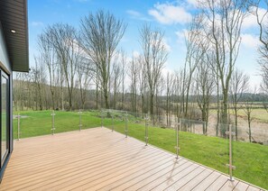 A wooden deck with a glass railing overlooking a grassy area with trees.