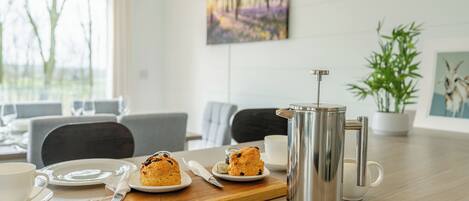 A dining area with a table set for breakfast, including a French press, plates with pastries, and cups.