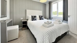 Een slaapkamer met een bed, nachtkastje, bankje en een raam met gordijnen.