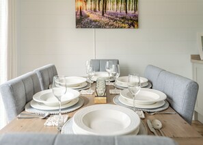 A dining table set with plates, glasses, and cutlery, surrounded by grey upholstered chairs, with a painting above.