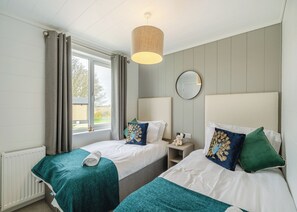 Une chambre avec deux lits, une fenêtre avec des rideaux, une table de chevet avec une lampe et un miroir au mur.