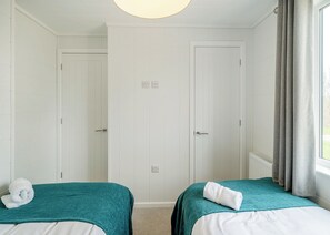 Quarto de hotel com duas camas, paredes brancas, uma janela com cortinas e uma luminária no teto.