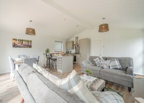 Una sala de estar moderna con un sofá gris, una mesa de comedor con sillas, una zona de cocina y un ventanal grande.