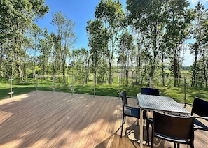 A wooden deck with a table and chairs, surrounded by trees and a clear sky.