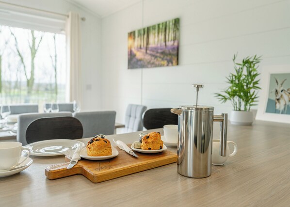 A dining area with a table set for breakfast, including a French press, plates with pastries, and cups.