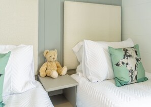 A bedroom with two beds, a nightstand, a teddy bear, and decorative pillows.