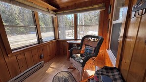 Interior acogedor de una cabaña con paredes de madera, ventanas amplias, un sillón mecedor y una mesa a cuadros.