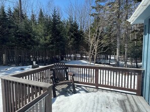 A wooden deck with a bench, surrounded by a snow-covered landscape and trees. - Loon Camp. (Rangeley)