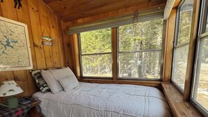 Un dormitorio de cabaña de madera con una cama, un mapa en la pared y una ventana con vista al bosque.
