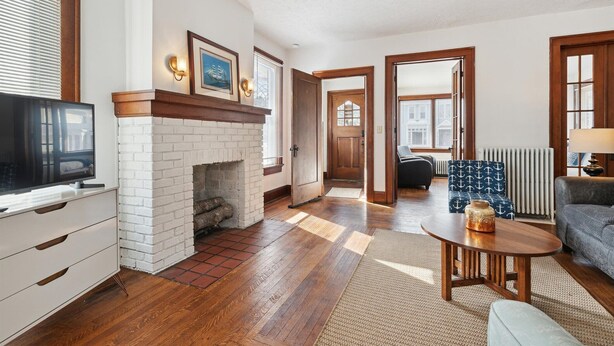 A living room with a fireplace, a television, and a seating area with a patterned ottoman. - Urban Roots — Mins from Cedar Point.  (Sandusky)