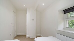 A bedroom with two single beds, a radiator, a window with a view of greenery, and a door. - Beacon Fell Cottage 2 (Longridge, Ribble Valley)