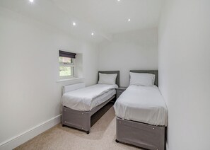 A small, clean room with two single beds, a window, and a radiator. - Beacon Fell Cottage 2 (Longridge, Ribble Valley)