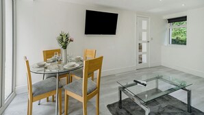 A modern dining room with a glass table, wooden chairs, and a vase with flowers. - Beacon Fell Cottage 2 (Longridge, Ribble Valley)