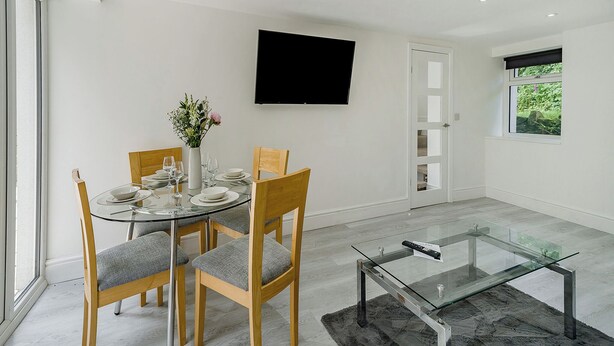 A modern dining room with a glass table, wooden chairs, and a vase with flowers. - Beacon Fell Cottage 2 (Longridge, Ribble Valley)