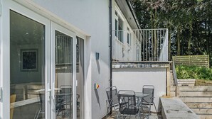 A building with a patio area featuring a table and chairs, a sliding glass door, and a small balcony with a railing. - Beacon Fell Cottage 2 (Longridge, Ribble Valley)