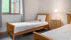 A single-bed room with a window, a bedside table with a lamp, and a nightstand.