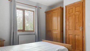 A bedroom with a bed, a window with curtains, a radiator, and wooden wardrobes.
