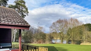 A building with a tiled roof, a wooden fence, and a grassy area with trees and a body of water.