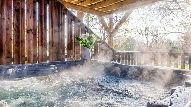A hot tub under a wooden pergola with steam rising, surrounded by trees. - 1 bedroom accommodation in Ely (Ely)
