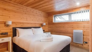 A wooden-paneled bedroom with a bed, bedside lamps, a heater, and a window with blinds. - 1 bedroom accommodation in Ely (Ely)