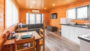 A wooden cabin interior with a dining area, sofa, kitchen, and large windows. - 1 bedroom accommodation in Ely (Ely)