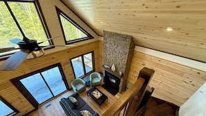 A high-ceilinged room with a fireplace, large windows, and a wooden interior. - Luxury Muskoka River Log Cabin (Bracebridge)