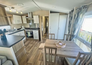 A compact kitchen with a stove, oven, and cabinets, a dining table with chairs, and a view through a window.