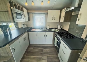A compact kitchen with a microwave, stove, sink, and cabinets. - This stunning holiday home with a double bedroom and en suite W. (Bishop Auckland)