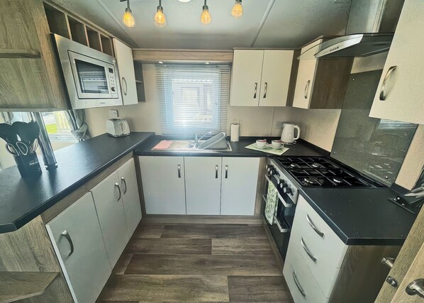 Une cuisine de taille réduite équipée d’un four à micro-ondes, d’une cuisinière, d’un évier et de placards.