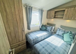 A compact bedroom with two beds, a wooden wardrobe, and a window with curtains.