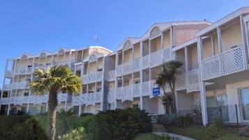 Un hôtel à plusieurs étages doté de balcons, de palmiers et d’un espace piscine.