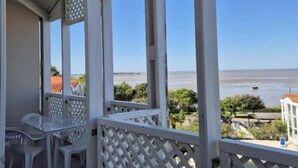 A covered outdoor area with a view of the beach, featuring a table and chairs, and a lattice railing. - Apartment with sea view and private pool (FOURAS)