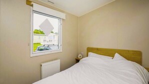 Ein Schlafzimmer mit einem Einzelbett, einem Fenster mit Blick auf ein Haus und Grünflächen sowie einem Nachttisch mit Lampe.