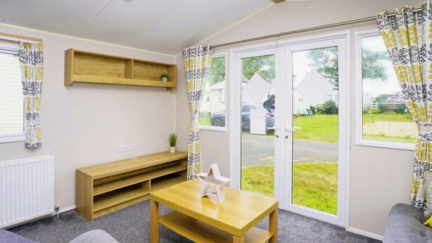 Ein Zimmer mit Holztisch, einer Bank, einem Sofa und einem Fenster mit Vorhängen.