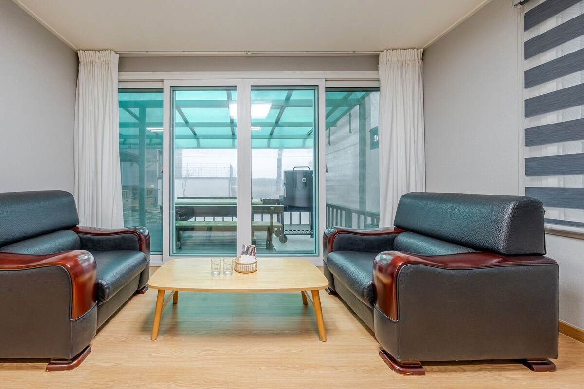 Une pièce comprenant deux fauteuils en cuir, une petite table en bois et une porte en verre donnant sur un espace extérieur.