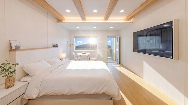 Ein modernes Schlafzimmer mit Bett, Nachttischen, einem Fernseher und Blick ins Freie.
