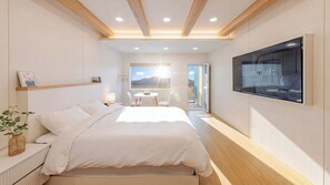 Un dormitorio moderno con cama, mesitas de noche, televisor y vistas al exterior.