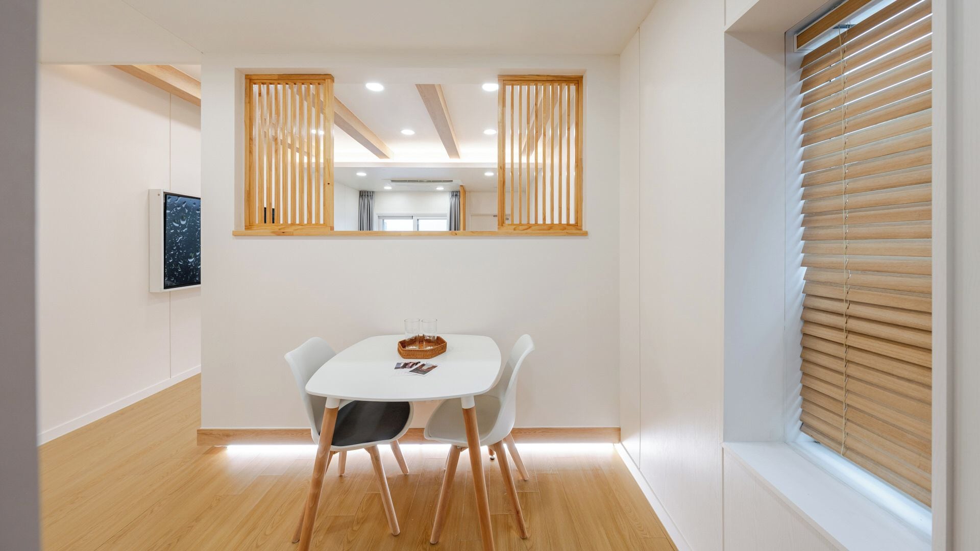 A dining area with a white table, two chairs, a basket, and a framed picture on the wall.