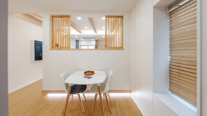 Un comedor con una mesa blanca, dos sillas, una cesta y un cuadro en la pared.