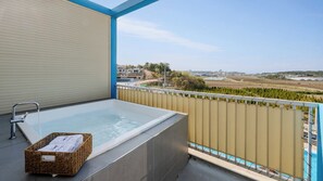 Un balcón con un jacuzzi, una cesta de mimbre y vistas a un paisaje con edificios y vegetación.