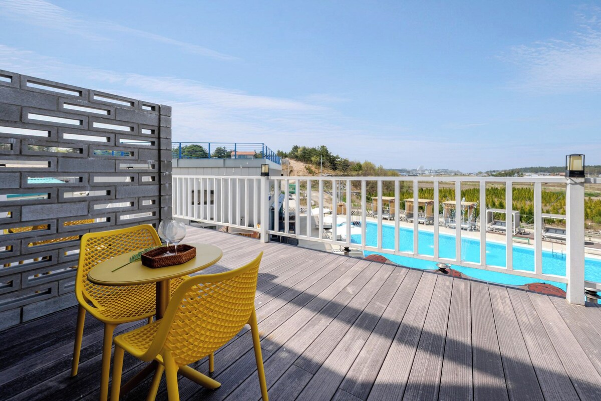 Une terrasse en bois avec une piscine, des chaises jaunes et une clôture blanche.